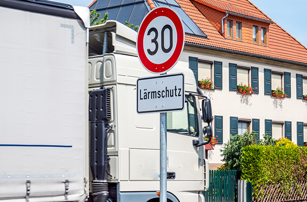Straßenschild Lärmschutz mit fahrendem LKW vor Stadthaus