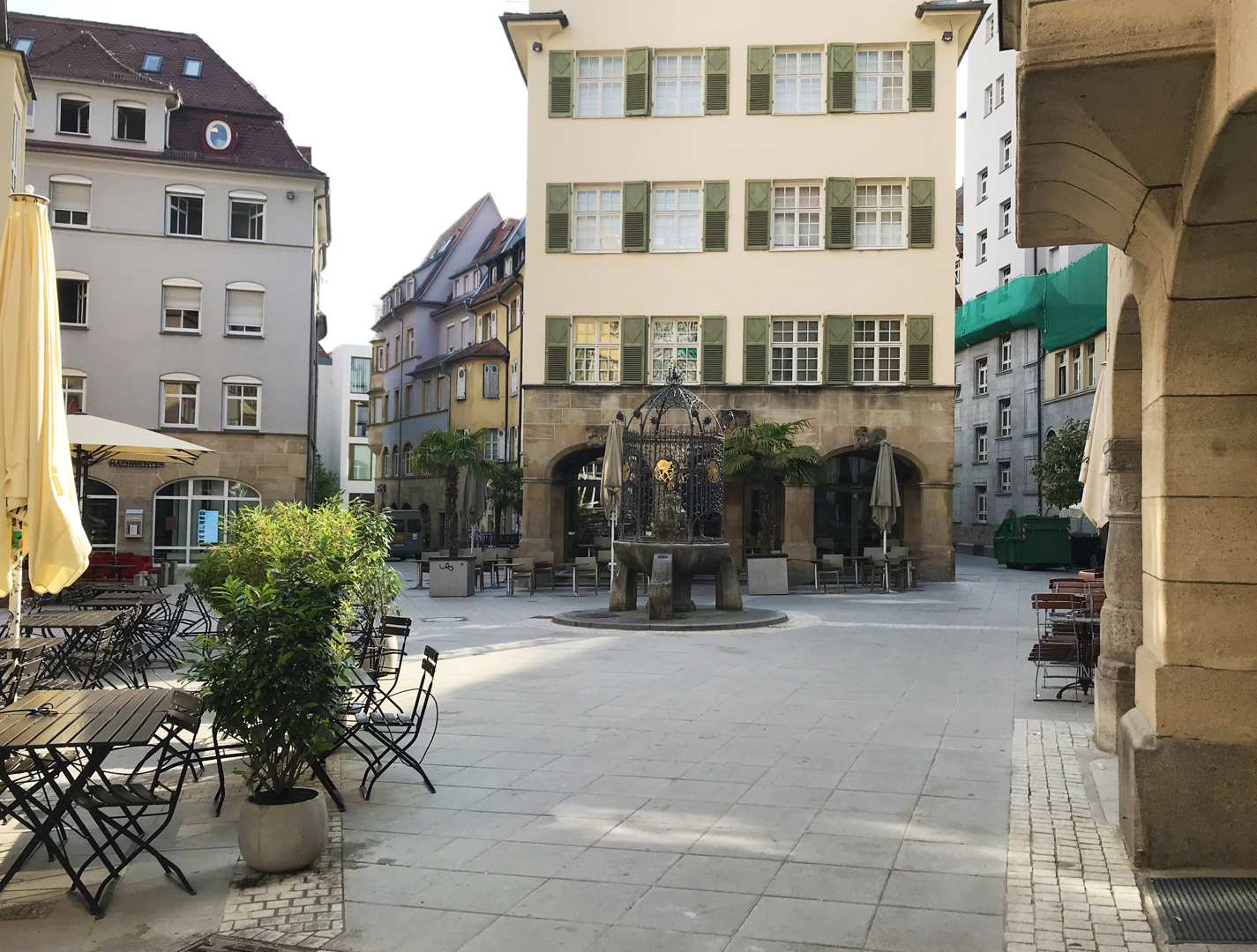 Der hans-im-Glück-Brunnen. Im Hintergrund ist die Café-Bar Deli zu sehen, links vorne die Außenbestuhlung der Kneipe Platzhirsch.