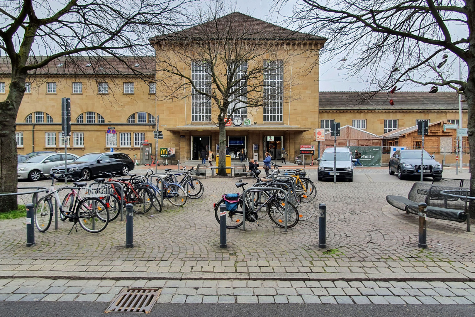 Zu sehen ist der Eingang zum Bahnhof und der Bahnhofsvorplatz in Bad-Cannstatt bei regenerischem Wetter und einigen Autos und Fahrrädern, die vor dem Eingang stehen. Foto: Stadt Stuttgart