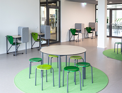 Ein Bereich zwischen den Klassenzimmern mit weißen Tischen und hellgrünen Stühlen mit Plätzen für Gruppen- und Einzelarbeit./Foto: Julian Rettig/Stadt Stuttgart